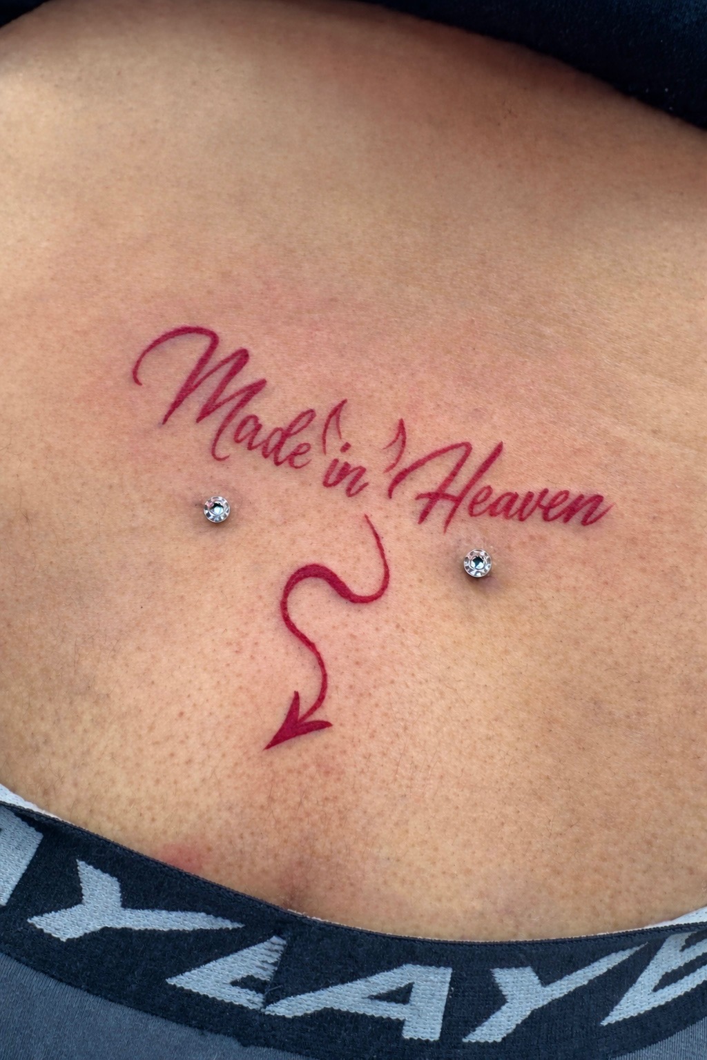 Red ink 'Made in Heaven' script tattoo with devil tail