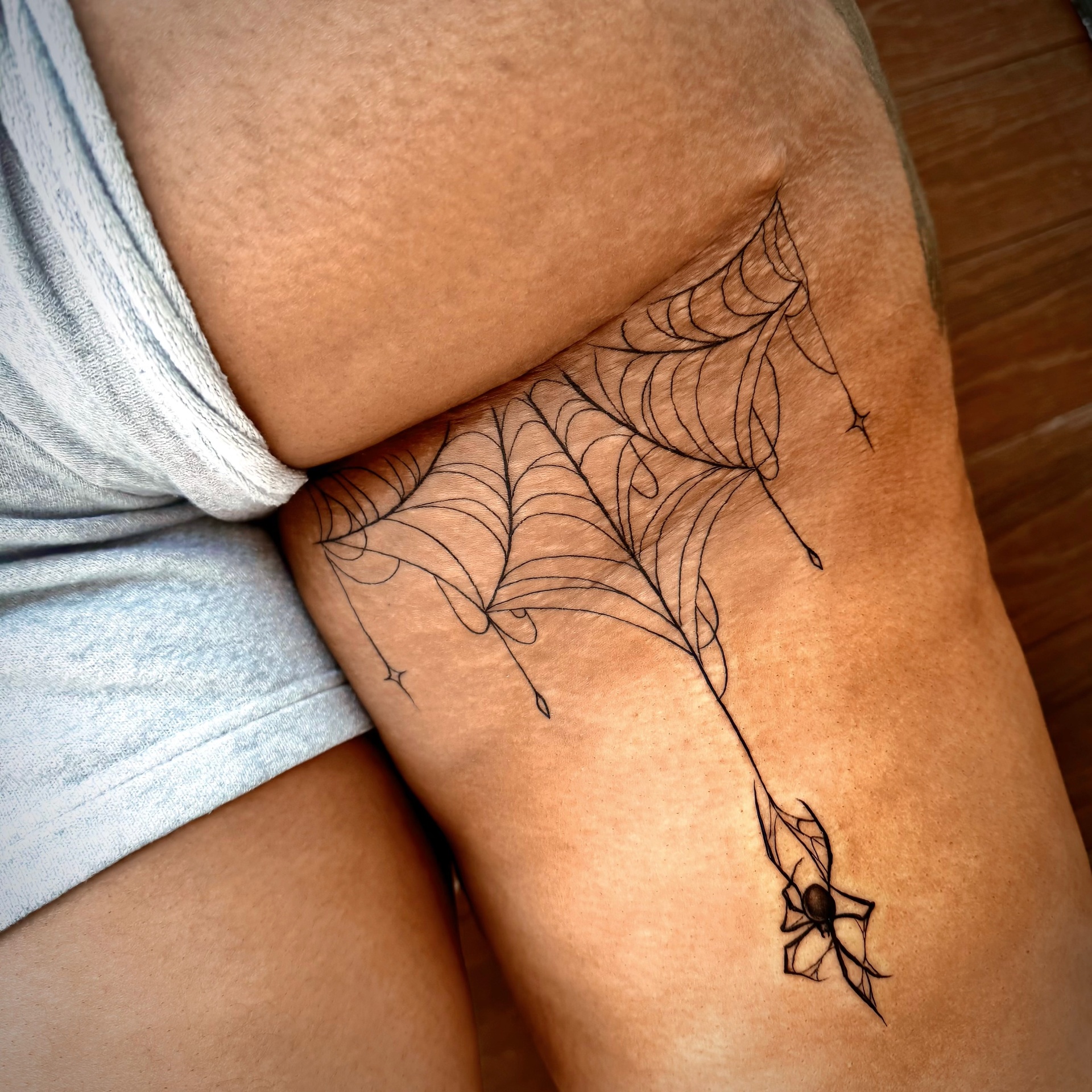 Fine-line spider web and spider thigh tattoo