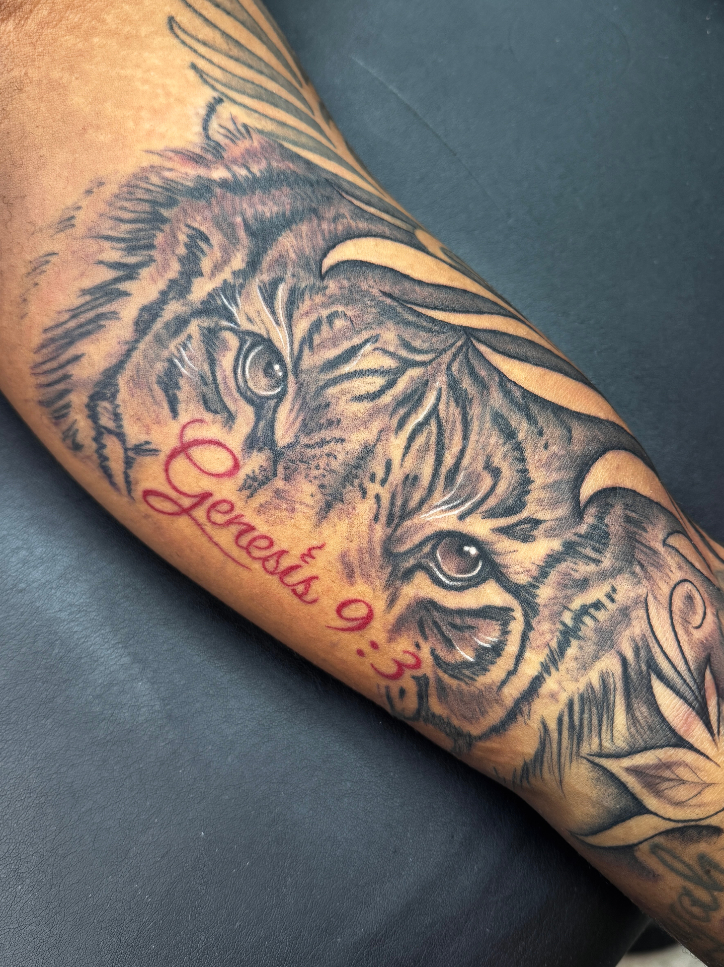 Realistic black and grey tiger forearm tattoo with red 'Genesis 9:3' script